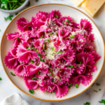 A plate of vibrant pink beetroot farfalle pasta topped with grated parmesan and chopped parsley
